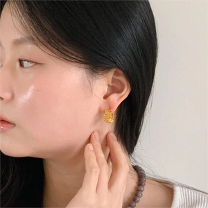 Close-up of golden textured hoop earrings featuring unique wrinkled surface on model
