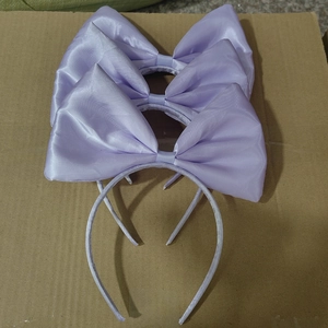 Three large purple satin bow headbands for girls displayed on a textured surface