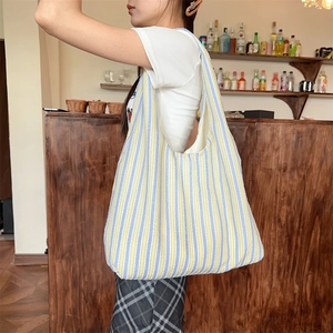 Detail of a large knitted striped tote bag with yellow and blue texture on a model