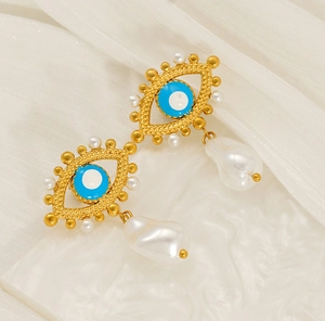 Macro detail of gold evil eye earrings featuring blue enamel and baroque pearls