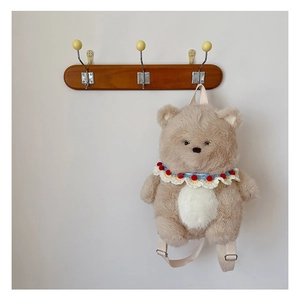 Close-up of plush teddy bear backpack with woven collar detail hanging on a wooden hook