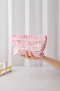 Pochette trucchi rosa con fiocchi e etichetta H&R BAG tenuta in mano da una modella