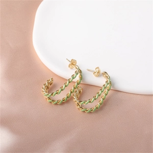 Detailed macro view of gold-tone rope twist earrings with green enamel on satin