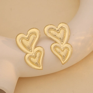 Elegant gold layered heart stud earrings with textured centers on white decor