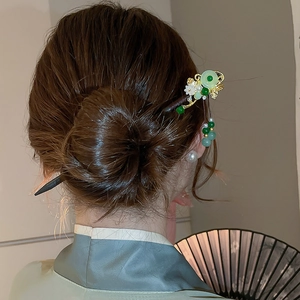 Detail of wooden hair stick with white flower, green jade beads and gold tassels on hair