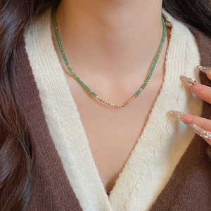Close-up of beaded necklace with green stone beads and golden metal accents on a model