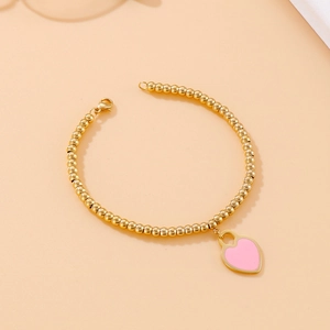 Detail of 18k gold plated beaded bracelet with pink enamel heart charm on orange background