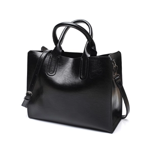 Detail view of a black glossy PU leather tote bag with sturdy handles and shoulder strap