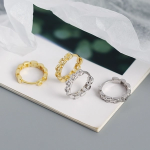 Detail shot of small gold and silver chain-link huggie earrings on white paper background
