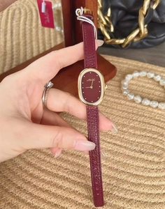 Close-up of a women's watch with an oval gold case and a burgundy leather strap on a wrist