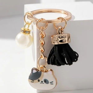 Macro detail of golden keychain featuring a spotted cat charm, black tassel and pearl bead
