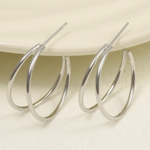 Macro detail of silver minimalist double-loop earrings on light yellow porcelain tray