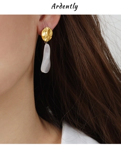 Dettaglio di orecchino d'oro elegante con pendente in resina bianca perlata a torsione