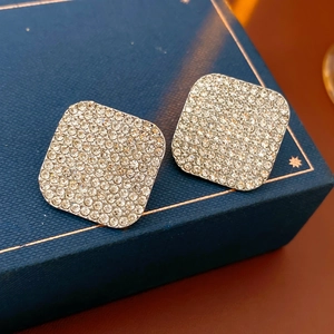 Macro shot of square crystal earrings with pavé diamonds on a blue jewelry box display