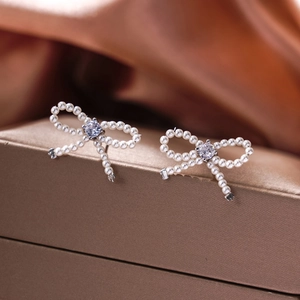 Elegant bow stud earrings with imitation pearls and zircon on bronze satin background