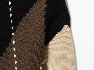 Detailed close-up of thick knit sweater with color-blocking and white V-shaped stitching