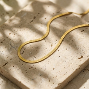 Detailed view of a gold herringbone snake chain placed on a beige travertine stone