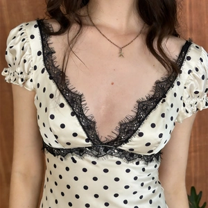 Dettaglio dell'abito beige a pois con scollo a V profondo e finiture in pizzo nero