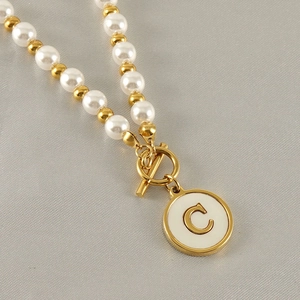 Detail of gold letter C pendant with white enamel on pearl and metal bead chain