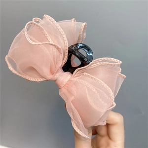 Detail of pink organza ribbon bow hair claw clip held by a hand on a grey background
