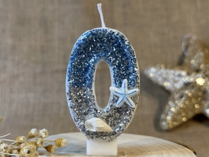 Detail of blue and silver glitter number 0 birthday candle with starfish and shells