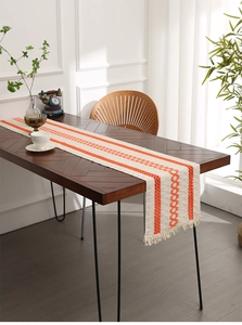 Close-up of beige linen table runner with orange geometric patterns and stylish tassels