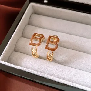 Golden B-letter earrings with brown enamel and bold chain link design on grey velvet