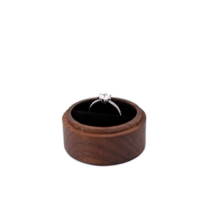 Top view of a round dark wood ring box with a silver diamond ring on black velvet