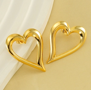 Detailed view of polished gold hollow heart-shaped earrings on cream textured background
