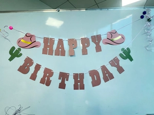 Detail of rose gold glitter Happy Birthday banner with pink cowboy hat and cactus accents