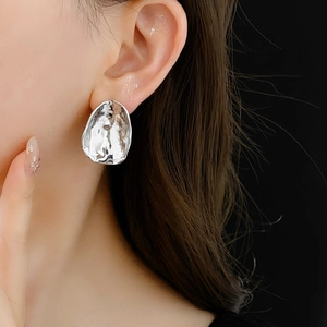 Close-up of a silver irregular round metal earring worn by a model on a black background