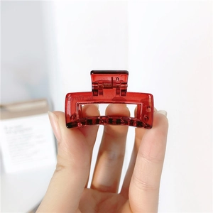 Detailed close-up of a small square transparent red hair claw clip held in hand