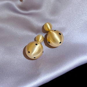 Close-up of 18k gold-plated brushed metal earrings with black polka dots on purple silk