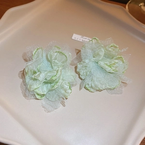 Close-up of light green lace flower earrings on a textured off-white display tray