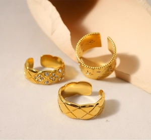 Dettaglio di tre anelli aperti dorati trapuntati con strass su uno sfondo beige
