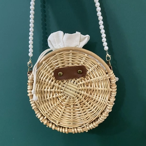 Top view of a round woven rattan bag with white drawstring lining and pearl chain strap