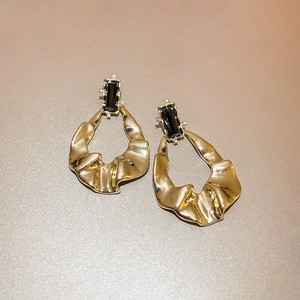 Detail of golden drop earrings with wavy metal plates and black gemstone accents