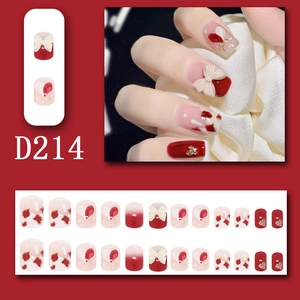 Detail of red press-on nails featuring 3D white bows, heart patterns, and gold foil accents