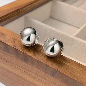 Minimalist silver spherical hoop earrings displayed on a rustic wooden jewelry box