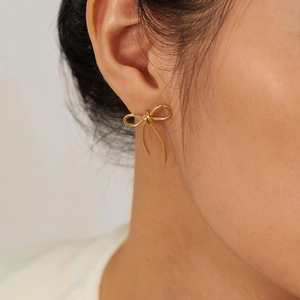 Close-up of stylish gold bow-shaped stud earrings worn by a model for a chic look
