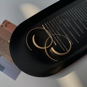 Detail of matte gold minimalist hoop earrings on a black decorative display tray