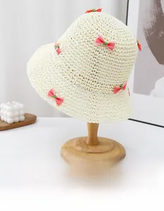 Détail du chapeau de paille crème avec des nœuds décoratifs roses et verts cousus