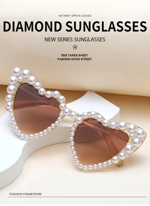 Detail of heart-shaped sunglasses featuring white pearl trim and brown gradient lenses