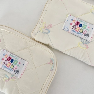 Detailed macro view of quilted cream pouches with embroidered bows and colorful labels