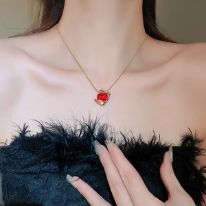 Close-up of a gold geometric necklace with a red stone pendant worn by a model