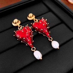 Detail of red heart baroque pearl earrings with gold plating on black leather