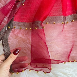 Detail of red silk scarf featuring golden metallic trim and small gold bead embellishments