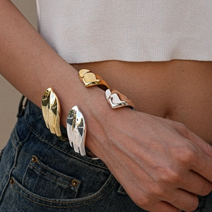 Detailed view of polished irregular open bangles in gold and silver on a female wrist