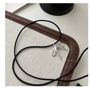 Detail of silver bow pendant on black cord necklace resting on a beige fabric tray