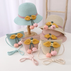 Detail of woven kids straw hat and matching bag with cherry pom-poms and yellow bow